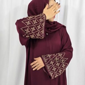 Abaya Grenat Bordeaux perlée avec manches ornées de perles dorées, accompagnée d’un foulard et d’une ceinture assortis.